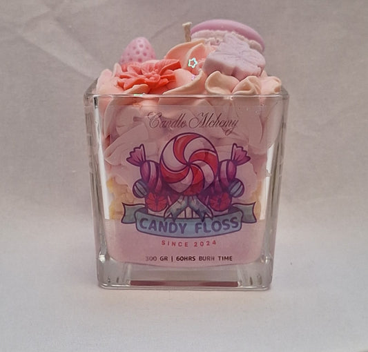 Handmade whipped wax dessert candle in glass jar with candy floss scent, topped with decorative sweets, macarons, and floral details.