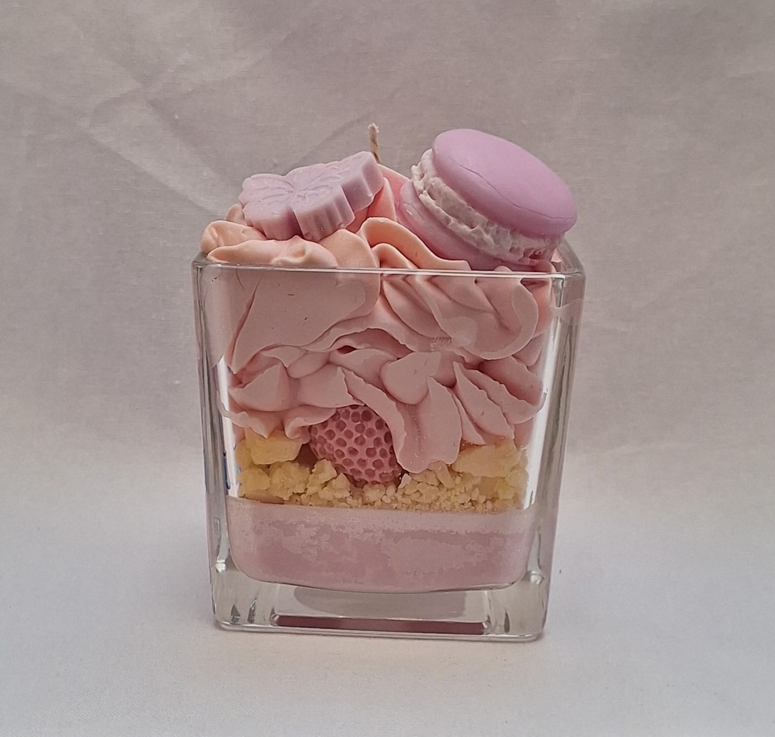 Handmade whipped wax dessert candle in glass jar with candy floss scent, topped with decorative sweets, macarons, and floral details.