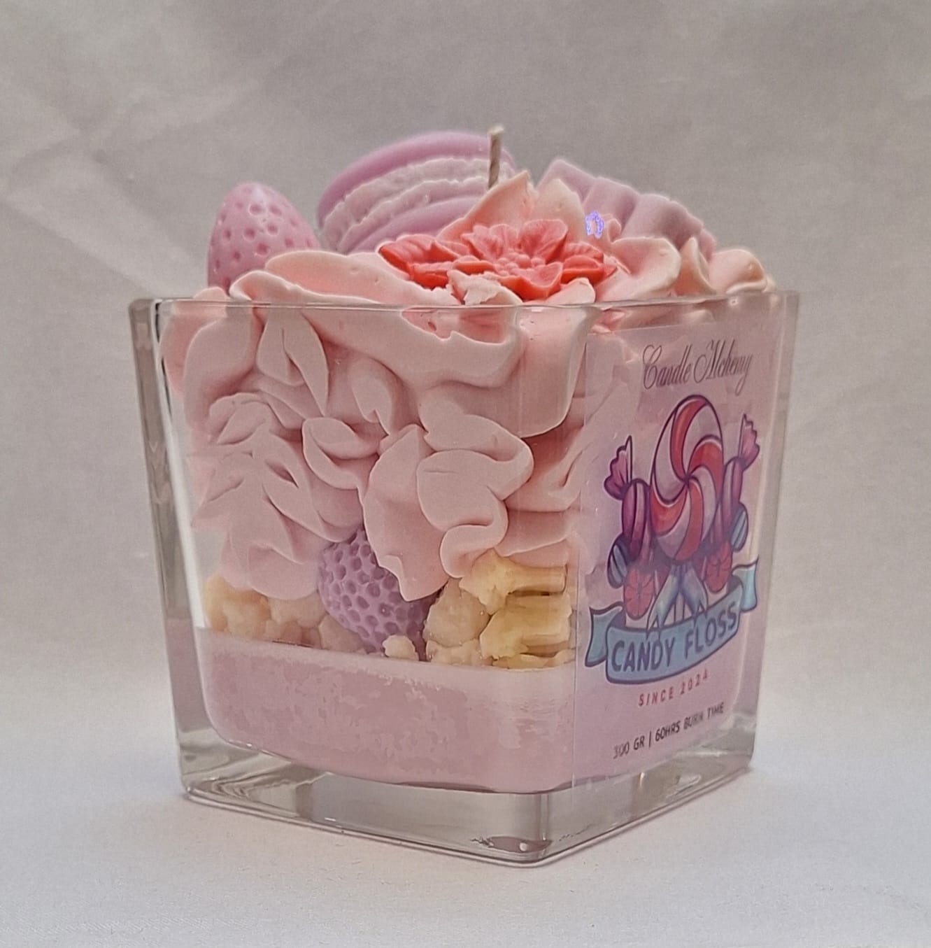 Handmade whipped wax dessert candle in glass jar with candy floss scent, topped with decorative sweets, macarons, and floral details.