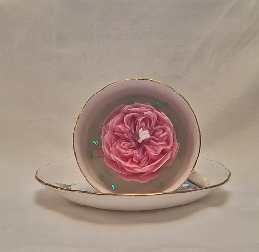 Top view of pink rose soy candle with green gem accents in vintage floral bone china teacup and saucer.