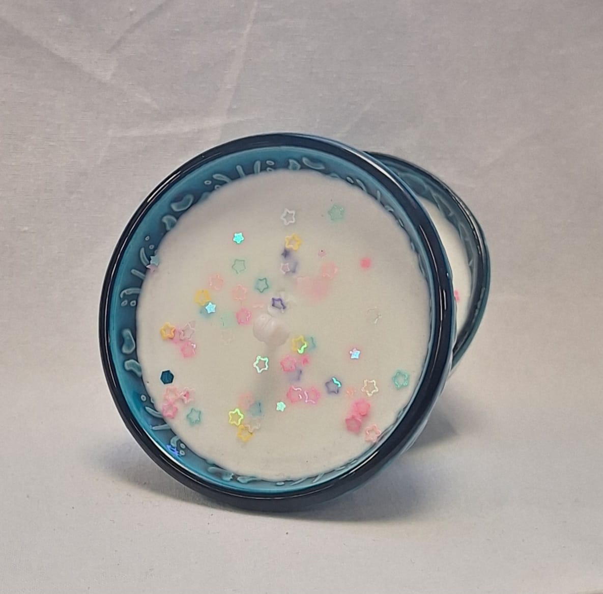 Hand-poured soy candle in blue glazed ceramic bowl with pastel star glitter topping for decorative home use or gifting.