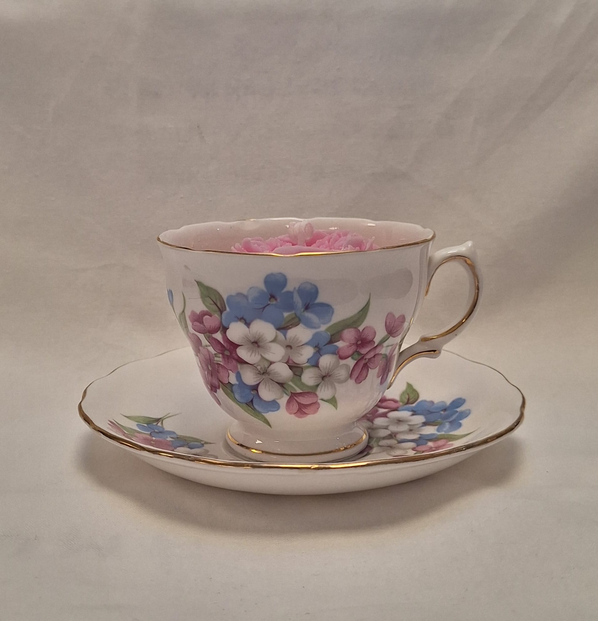 Side view of vintage floral teacup candle with blue, pink, and white flower design on bone china with gold trim.